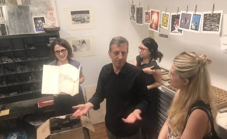 A photo of a person talking to other people while showing them a print sample.