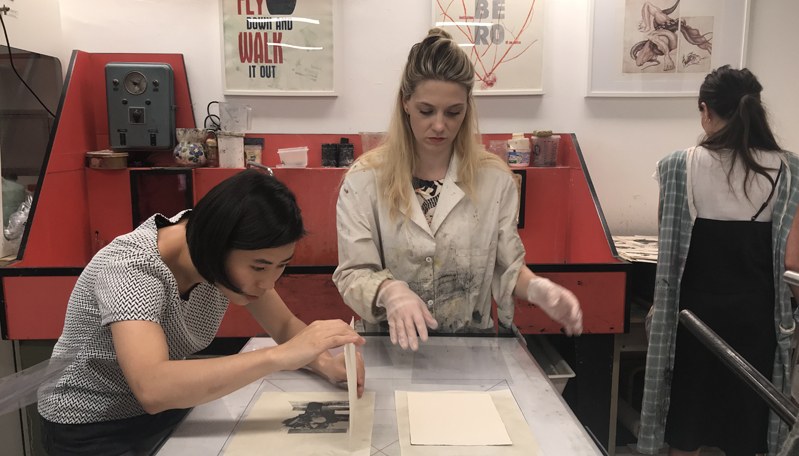 A photo of two women making some imprinted designs on paper with typography ink.