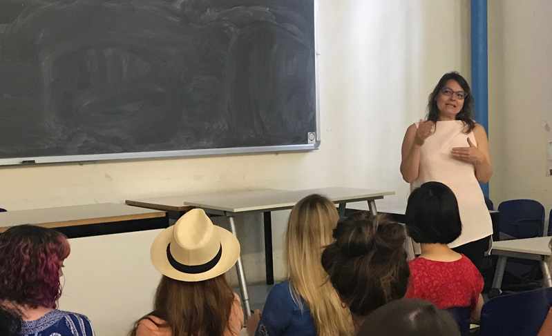 A group of people sitting in a classroom and listening to a lecture given by a woman.