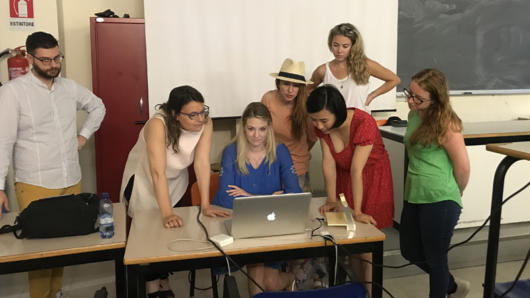 A photo of a group of people standing around a desk and checking something on a laptop.