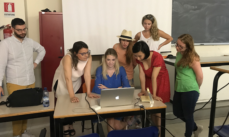 A photo of a group of people standing around a desk and checking something on a laptop.