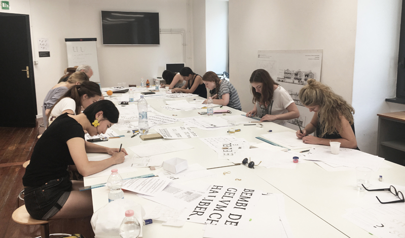 A photo of a group of students working at a table, trying to draw letters for the typography course.