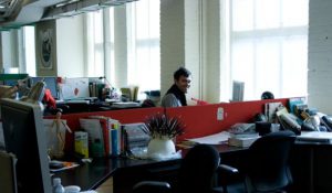A photograph of a man behind a working desk.