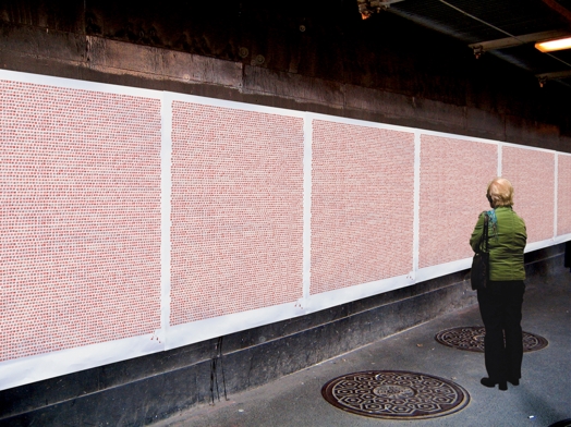 A woman in a green coat starring at a wall depicting some squares made from red text characters.