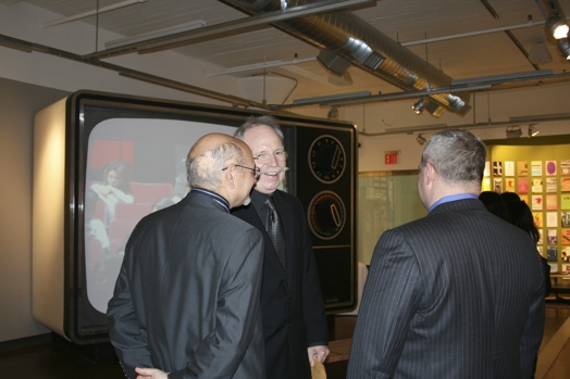 Photograph of three men in front of an old tv set.