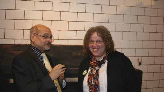 Photograph of a man and a woman in front of a white wall.
