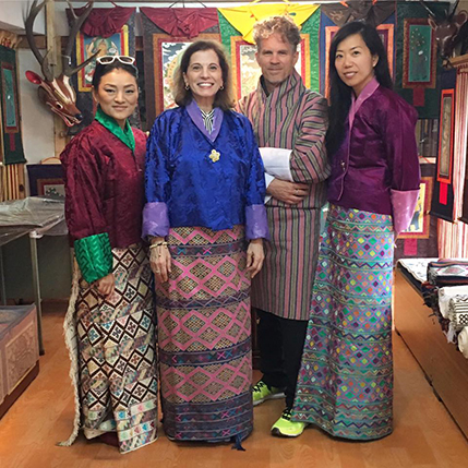 A photo of a group of people dressed in some colorful traditional clothes while standing in some art workshop.