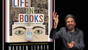 A photo of a man with his raised hands and standing near a poster showing an opened book and a drawn face on it. On the book ther is a title that says: Life in Books. Warren Lehrer.