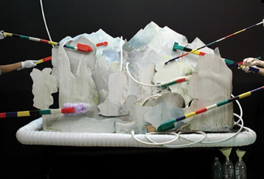 A photo of an art setup depicting a white plate with foam and paper on it, that has different striped colored straws and cables pinned in it.
