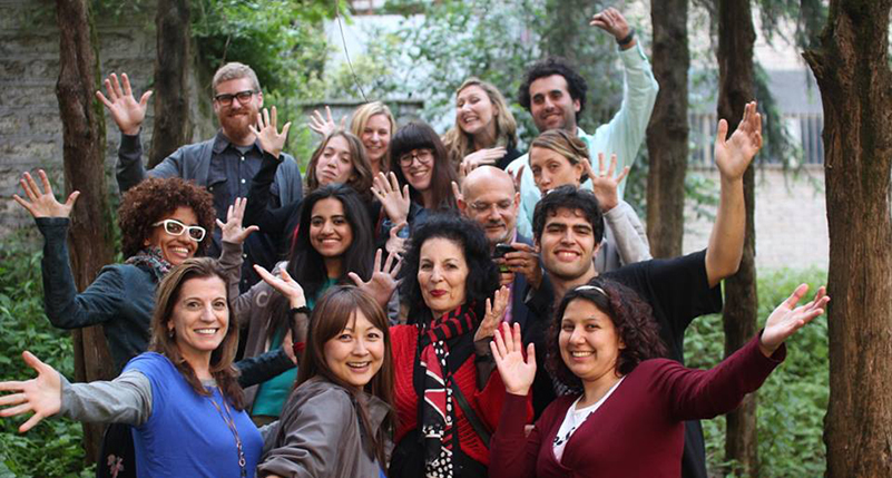 A photo of a group of people sitting in a green park with their hands up.