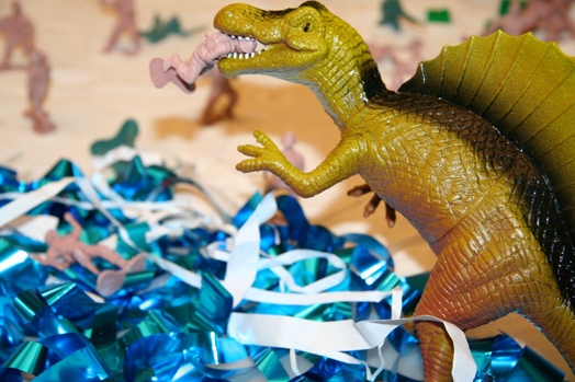 A photo showing a plastic dinosaur eating a plastic toy soldier and some blue and white ribbons.