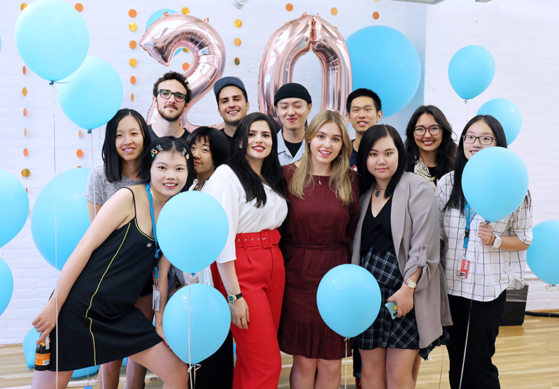 A photo of a group of students surrounded by blue balloons and in the background the number twenty made also from shiny balloons.