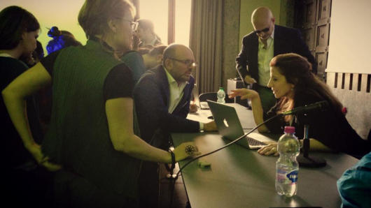 A photo of a group of people discussing something and looking at a laptop.