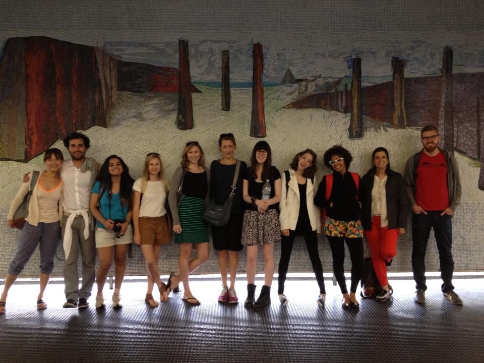 A photo of a group of students standing in a hall way and behind them there is a wall art work.