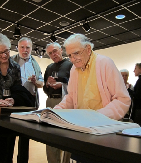 A group of old people staring at  a design book on a table.