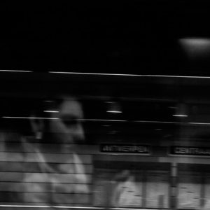 A black and white photo of a man's reflection on a window while passing some building.