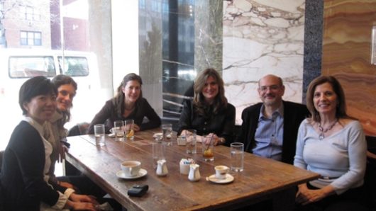 A photo of a group of people sitting at a table with glasses and coffee cups on it.