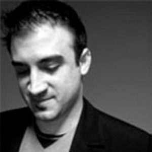 A black and white photo of a man wearing a suit and a blouse looking down.