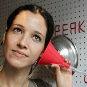 A photo of a woman holding a red funnel whit a transparent tube against her ear.