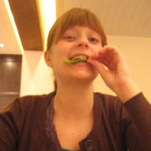 A photo of a woman eating a green vegetable and wearing a black blouse.
