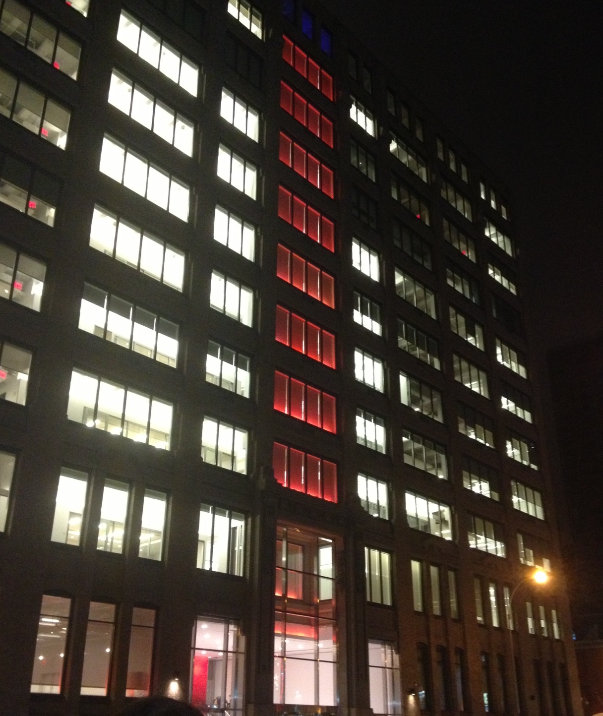 A nightly photo of an illuminated building with white lights and the middle of it is illuminated by red lights.