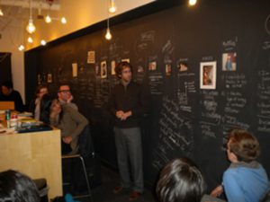 A photo of a group of people sitting in front of a black wall with white writings and photos on it.