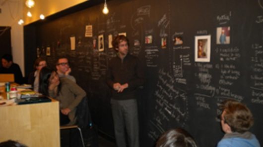 A photo of a group of people sitting in front of a black wall with white writings and photos on it.