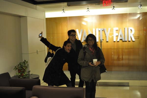 A photo of three people in front of a Vanity Fair 3d logo on a wall.