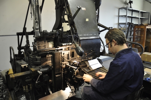 A photo of a man making some text for a printing press.