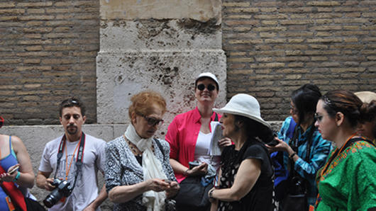 A photo of a group of people in the street near a brick wall.