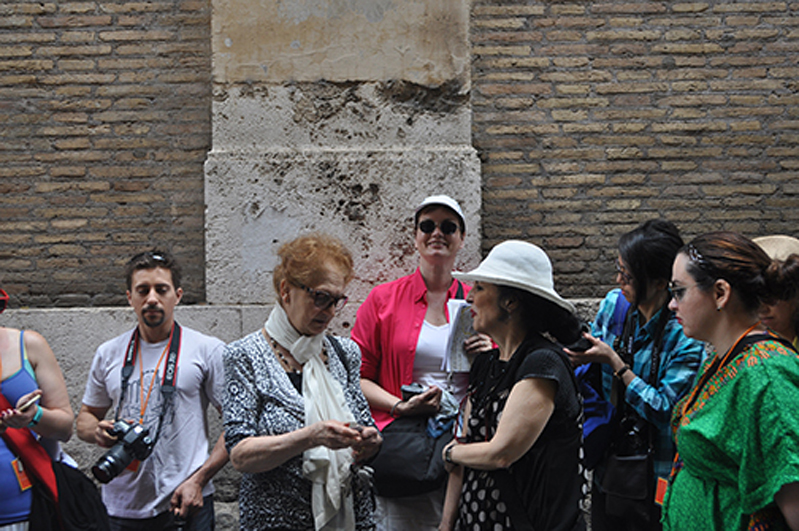 A photo of a group of people in the street near a brick wall.