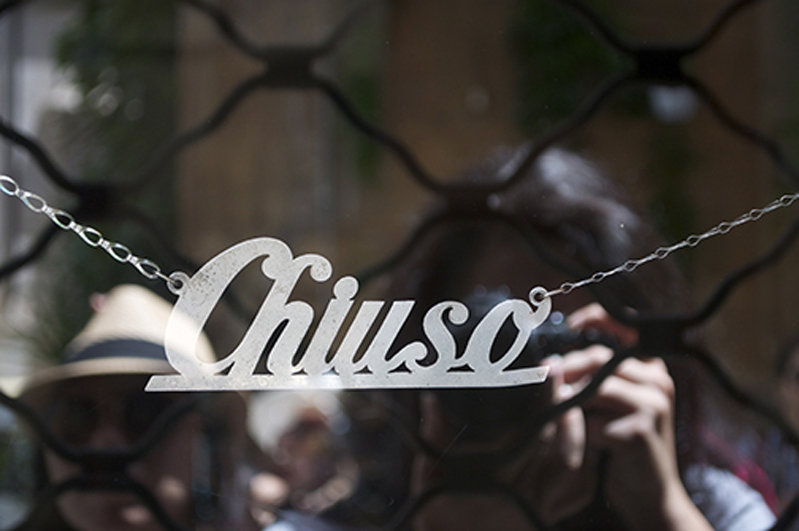 A photo of a text logo held by chains. The text says: Chiuso.