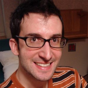 A photo of a man wearing glasses and a red shirt with gray lines.