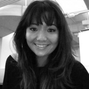 A black and white photo of a smiling woman while sitting in an office.