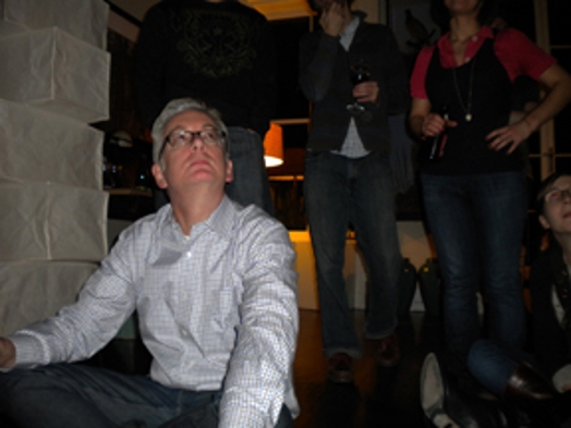 A photo of a man in a white shirt and glasses, sitting near some other people and look up.