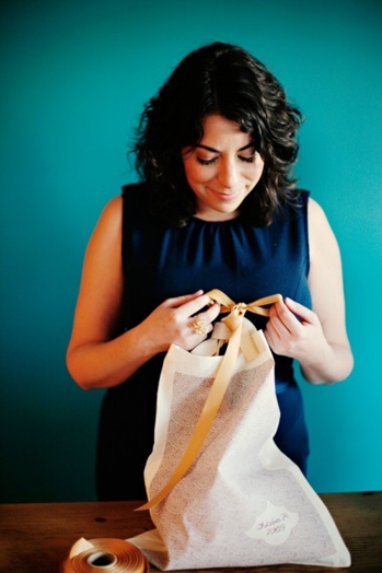 A woman dressed in a blue dress is making a bow from a yellow ribbon for a tissue bag.