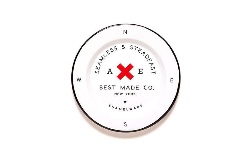 A white plate with a black rim, the four cardinal points, a red X in the middle and around it the text: SEAMLESS & STEADFEST A X E BEST MADE CO NEW YORK.