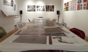 A photo of an art workshop with a table in the middle on which are different printed posters.