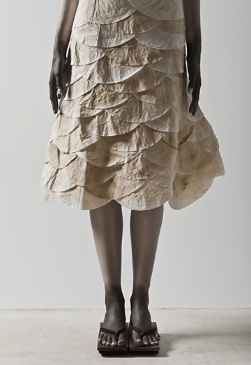 A lower part of a woman wearing a paper like cream dress.