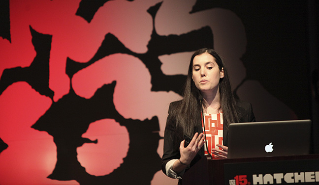 A photo of a woman giving a lecture at a stand.