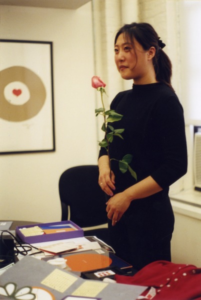A photo of a woman standing and holding a rose in her hand.