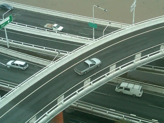 An aerial photo of a segment of highways, suspended road connections and some cars passing.