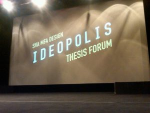 A photo of a stage and a projector screen with text: SVA MFA DESIGN IDEOPOLIS THESIS FORUM.