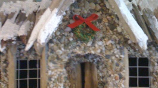 A photo of what looks like a gingerbread house with red ribbon and green mistletoe on it.