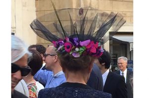 A photo of a lady's hat with colorful flowers around it. Also there are other people walking by her.