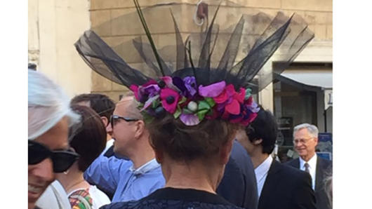 A photo of a lady's hat with colorful flowers around it. Also there are other people walking by her.