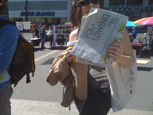 A photo of a girl reading a flyer on the street.