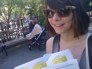 A photo of a girl with sun glasses reading a flyer on the street.