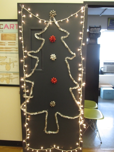 A photo of Christmas light strips on a door along a silver garland that forms a Christmas tree.