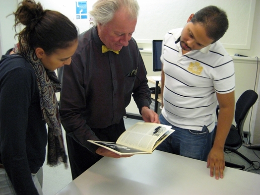 A photo of a group of people looking trough an artbook and reading the content.